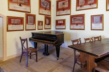 Tarihi odada, çerçeveli sanat eserleri ve ahşap mobilyalarla klasik ahşap piyano. 18 Mart 2025, Madalyon, Çek Cumhuriyeti.