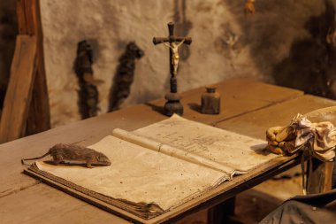 Açık kitap, sıçan, haç ve eldivenlerin tozlu masada olduğu klasik bir çalışma. 18 Mart 2025, Madalyon, Çek Cumhuriyeti.