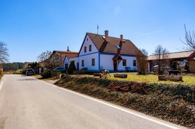Açık mavi gökyüzü ve ağaçlarla güneşli bir günde kır evi. 21 Mart 2025, Holasovice, Çek.