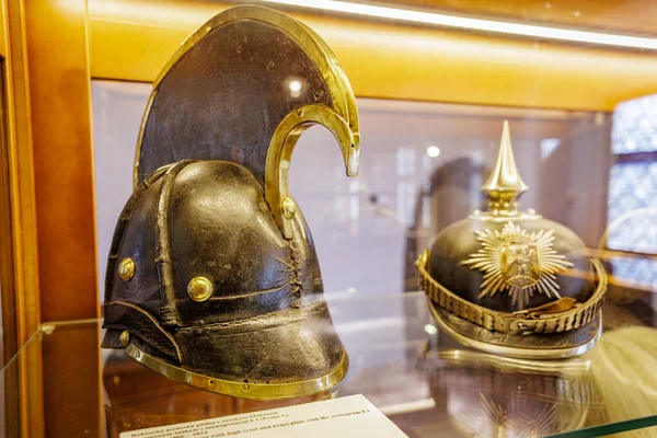 Tarihi miğferler sergileniyor: Eski Yunan korint ve prusyan Pickelhaube cam kutuda. 18 Mart 2025, Madalyon, Çek Cumhuriyeti.