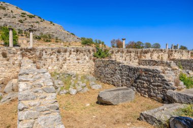 Ortasında büyük bir kaya olan taş bir duvar. Duvar eski ve üzerinde bir sürü yosun yetişiyor. Gökyüzü açık ve mavi. Yunanistan 'ın antik Filippi kentinin kalıntıları