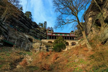 Sonbahar yaprakları arasında mavi gökyüzü ile kayalık bir araziye inşa edilmiş tarihi dağ kulübesi..