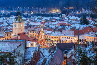 Ortasında Noel ağacı olan bir şehir. Ağaç ışıklarla çevrili ve insanlar etrafında toplanıyor.