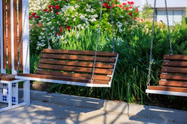Tahta bahçe salıncak, parlak bir çiçek arka planıyla güneşli bir günde.