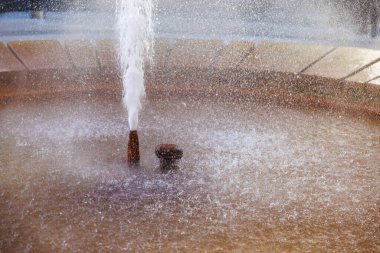 Güneşli park ortamında akan suyu olan dairesel taş çeşme, doğal gayzer..