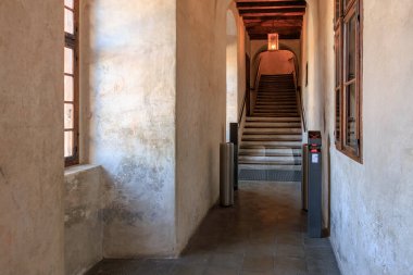 Güneşli koridorda sıcak tonlu ve geniş pencereli tarihi taş merdiven. 20 Mart 2025, Cesky Krumlov, Çek.