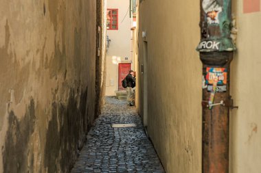 Avrupai dar bir sokak, kaldırım taşı sokağında oturan bir erkek. 20 Mart 2025, Cesky Krumlov, Çek.