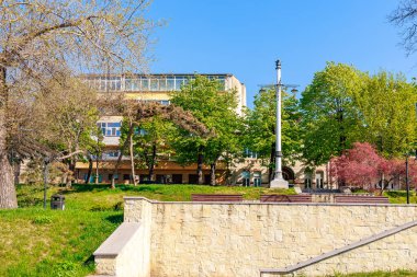 Yeşil ağaçlar ve taş anıtlarla dolu şehir parkında bahar günü. 3 Mayıs 2025 Romanya.