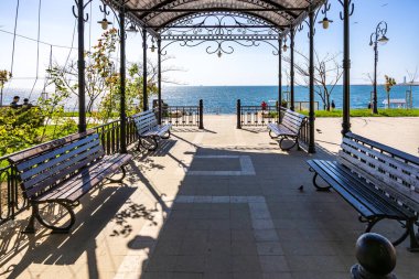 Güneşli bir günde dekoratif demir tepe örtüsünün altında banklarla deniz kenarında gezinti. 3 Mayıs 2025 Romanya.