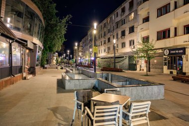 Sessiz mahalledeki boş sokak ve açık kafeli gece şehir manzarası. 3 Mayıs 2025 Romanya.
