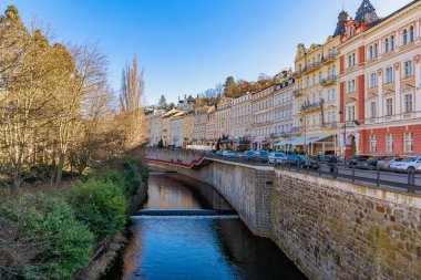 Canlı bir sokak sahnesinde nehir boyunca tarihi binaları olan Avrupa 'nın resmi bir kasabası. 18 Mart 2025, Karlovy Vary, Çek Cumhuriyeti.