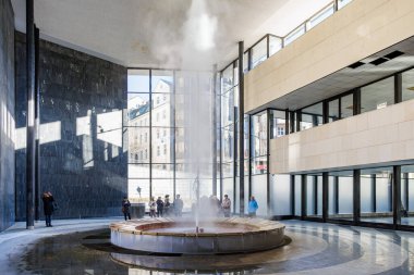 Jeotermal kaynak çeşmesi modern mimari alanda ziyaretçilerle birlikte kapalı bir yerde. 18 Mart 2025, Karlovy Vary, Çek Cumhuriyeti.
