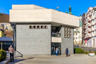 Şehir merkezindeki modern taş bina yakınındaki insanlarla dolu. 18 Mart 2025, Karlovy Vary, Çek Cumhuriyeti.