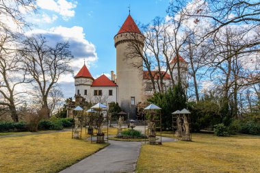 Mavi gökyüzünün altındaki sakin bahçelerde kırmızı çatıları olan tarihi Avrupa şatosu. 17 Mart 2025, Konopiste Şatosu, Çek Cumhuriyeti.