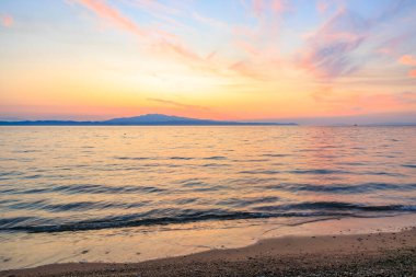Okyanus sakindir ve gökyüzü pembe ve turuncu renklerin güzel bir karışımıdır. Arka planda güneş batarken manzara sakin ve huzurlu.
