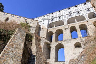 Mavi gökyüzüne karşı taş kemerler ve heykeller olan tarihi şato kompleksi.