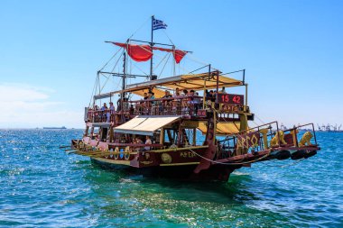 Kırmızı yelkenli ve beyaz tenteli büyük bir tekne okyanusta yüzüyor. Tekne insan kaynıyor ve teknede birkaç bayrak var. 8 Ağustos 2024 Selanik Yunanistan