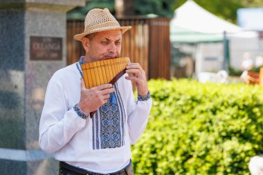 Geleneksel işlemeli gömlekle flüt çalan yaşlı beyaz bir erkek. 22 Mayıs 2025 Balti Moldova.