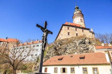 Cesky Krumlov 'da mavi gökyüzünün altında haç heykeli olan tarihi şato. 20 Mart 2025, Cesky Krumlov, Çek.