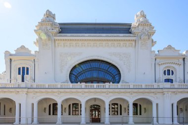 Süslü mimarisi ve açık mavi gökyüzünün altında kemerli pencereleri olan büyük tarihi beyaz bina. 3 Mayıs 2025 Romanya.