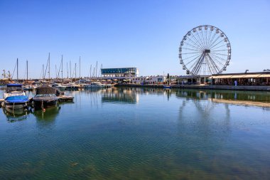 Güneşli bir liman sahnesi, dönme dolap ve açık bir günde tekneler. 3 Mayıs 2025 Romanya.