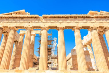 Parthenon 'un sütunları tamir ediliyor. Gökyüzü açık ve mavi. Sütunlar taştan yapılmıştır.