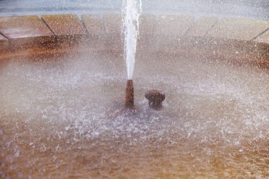 Çeşme suyu dairesel havuza sıçrıyor. Etrafı sis ve taşla çevrili. Doğal gayzer..