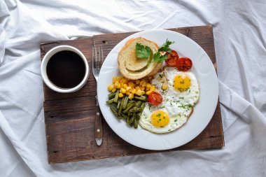 Yatakta kahvaltı. Domatesli sahanda yumurta, yeşil fasulye, mısır ve tost. İngiliz vejetaryen kahvaltısı. Üst görünüm.