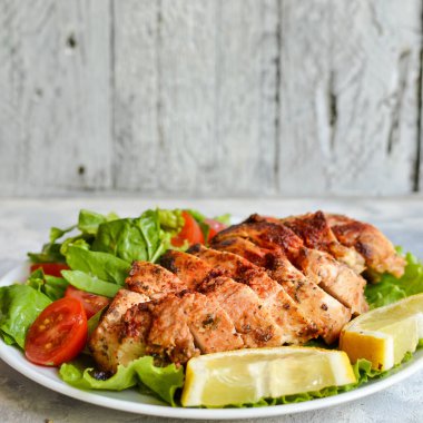 Ispanak ve domatesli ızgara tavuk göğsü salatası. Sağlıklı şekilde kızarmış tavuk göğsü, limon, kiraz domatesleri, ıspanak ve marul yiyor. Hafif arkaplan.