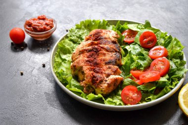 Ispanak ve domatesli ızgara tavuk göğsü salatası. Sağlıklı şekilde kızarmış tavuk göğsü, limon, kiraz domatesleri, ıspanak ve marul yiyor. Koyu arkaplan.