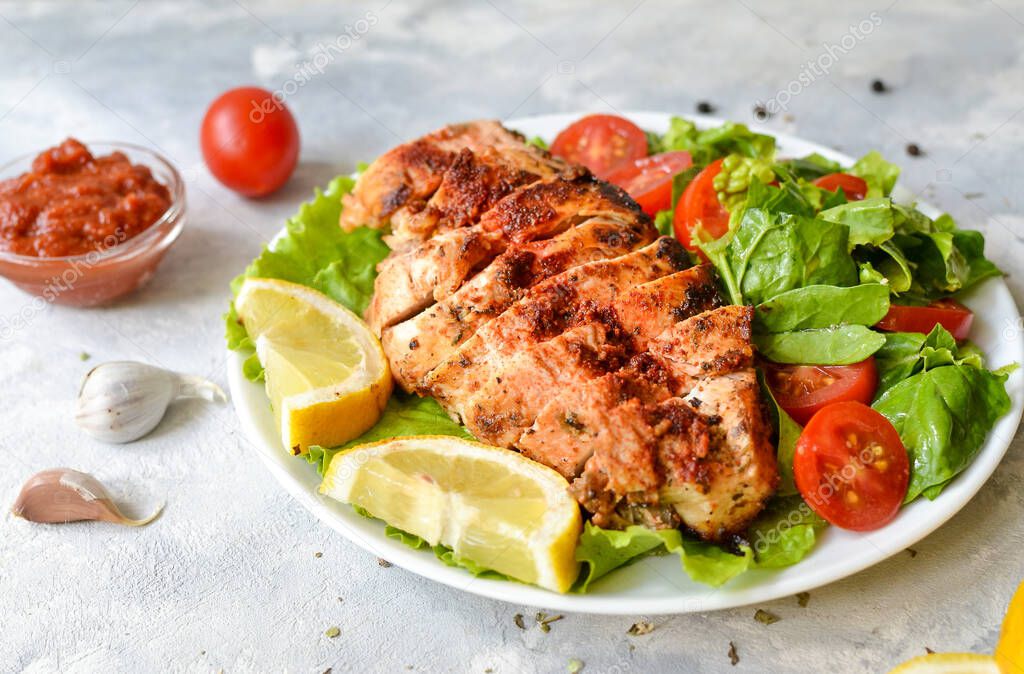 Grilled chicken breast salad with spinach and tomatoes. Healthy eating Fried chicken breast, lemon, cherry tomatoes, spinach and lettuce. Light background.