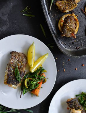 Limonlu ızgara balık, şifalı ot ve biberiye. Beyaz tabakta kızarmış balık filetosu. Güzel bir yemek sunumu. Rucolla salatası ve havuç. Üst görünüm