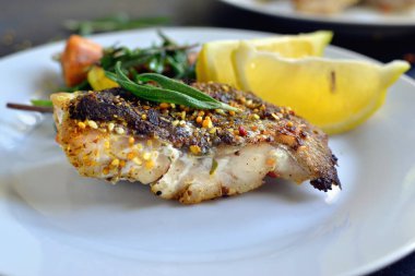 Limonlu ızgara balık, şifalı ot ve biberiye. Beyaz tabakta kızarmış balık filetosu. Güzel bir yemek sunumu. Rucolla salatası ve havuç. Yakın plan..