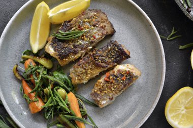 Limonlu ızgara balık, şifalı ot ve biberiye. Gri tabakta kızarmış balık filetosu. Güzel bir yemek sunumu. Rucolla salatası ve havuç. Yakın plan. Koyu arkaplan