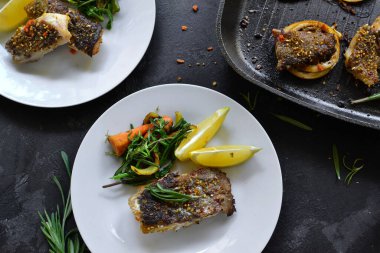Limonlu ızgara balık, şifalı ot ve biberiye. Beyaz tabakta kızarmış balık filetosu. Güzel bir yemek sunumu. Rucolla salatası ve havuç. Üst görünüm