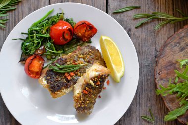 Limonlu ızgara balık, şifalı ot ve biberiye. Beyaz tabakta kızarmış balık filetosu. Güzel bir yemek sunumu. Rucolla salatası ve havuç. Üst görünüm