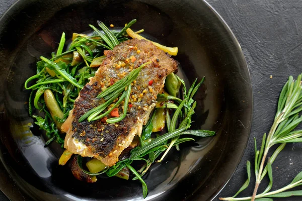 Limonlu ızgara balık, şifalı ot ve biberiye. Siyah tabakta kızarmış balık filetosu. Güzel bir yemek sunumu. Rucolla salatası ve havuç. Yakın plan. Koyu arkaplan