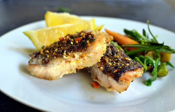 Limonlu ızgara balık, şifalı ot ve biberiye. Beyaz tabakta kızarmış balık filetosu. Güzel bir yemek sunumu. Rucolla salatası ve havuç. Yakın plan..