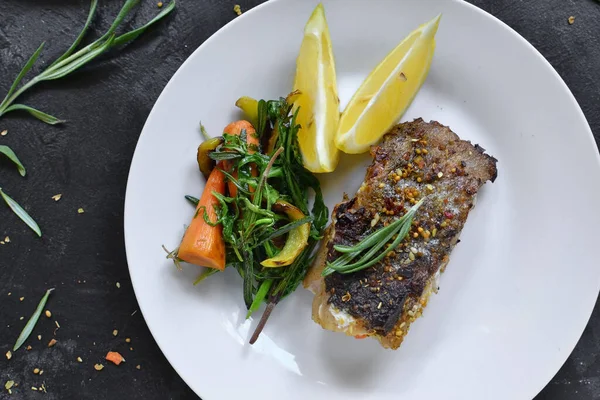 Limonlu ızgara balık, şifalı ot ve biberiye. Beyaz tabakta kızarmış balık filetosu. Güzel bir yemek sunumu. Rucolla salatası ve havuç. Üst görünüm