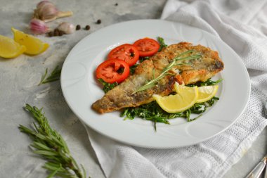 Domatesli, limonlu ve biberiyeli kızarmış balık filetosu. Beyaz tabak. Hafif arkaplan. Beyaz keten peçete..