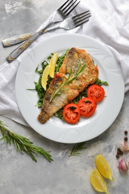 Domatesli, limonlu ve biberiyeli kızarmış balık filetosu. Beyaz tabak. Hafif arkaplan. Beyaz keten peçete..