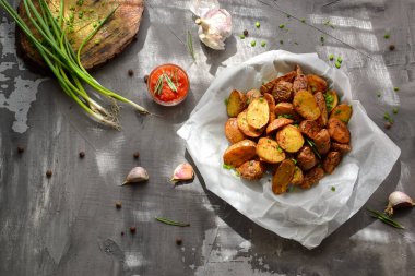 Köy patatesleri. Yeşil soğanlı fırında patates ve parşömende otlar. Gri arka plan. Lezzetli bir akşam yemeği. Üst Manzara. Yatay görünüm