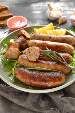 Limonlu ve ketçaplı ızgara sosis. Bitki ve biberiyeli Bavyera sosisi. Gri koyu arka plan. Gri tabak ve keten peçete.