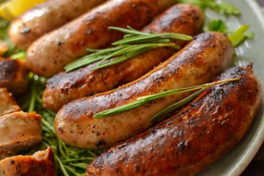 Limonlu ve ketçaplı ızgara sosis. Bitki ve biberiyeli Bavyera sosisi. Gri koyu arka plan. Gri tabak ve keten peçete. Yakın çekim.