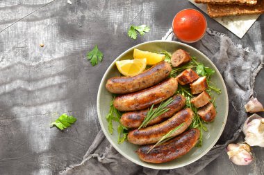 Limonlu ve ketçaplı ızgara sosis. Bitki ve biberiyeli Bavyera sosisi. Gri koyu arka plan. Gri tabak ve keten peçete.