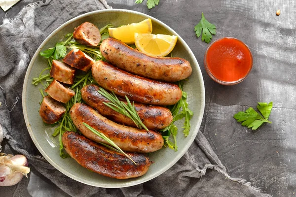 Limonlu ve ketçaplı ızgara sosis. Bitki ve biberiyeli Bavyera sosisi. Gri koyu arka plan. Gri tabak ve keten peçete.