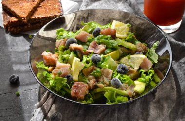 Salata, marul, balık, yabanmersini, limon ve avokado. Sağlıklı öğle yemeği ya da brunch. Karanlık arka plan. Keten gri peçete. Siyah cam tabakta salata. Arka ışık. Avokado ile balık kasesi. Üst görünüm.