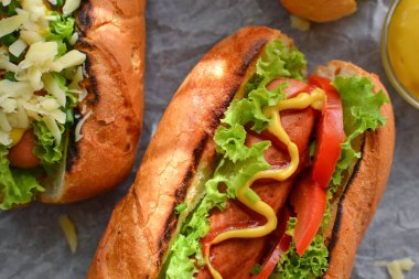 Bir sosisli, hardallı ve ketçaplı, marullu, peynirli ve sosisli. Karanlık arka plan. yemek arkaplanı fotokopi alanı. Yakın plan. Üst görünüm