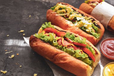 Çeşitli dolgulu sosisliler. Karanlık arka plan. yemek arkaplanı fotokopi alanı. Hardallı, ketçaplı, marullu, peynirli ve domatesli sosisli sandviç. Kapat.