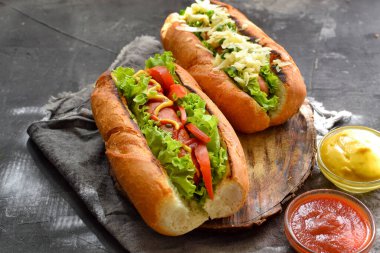 Çeşitli dolgulu sosisliler. Karanlık arka plan. yemek arkaplanı fotokopi alanı. Hardallı sosisli, ketçaplı, marullu, peynirli ve domatesli..